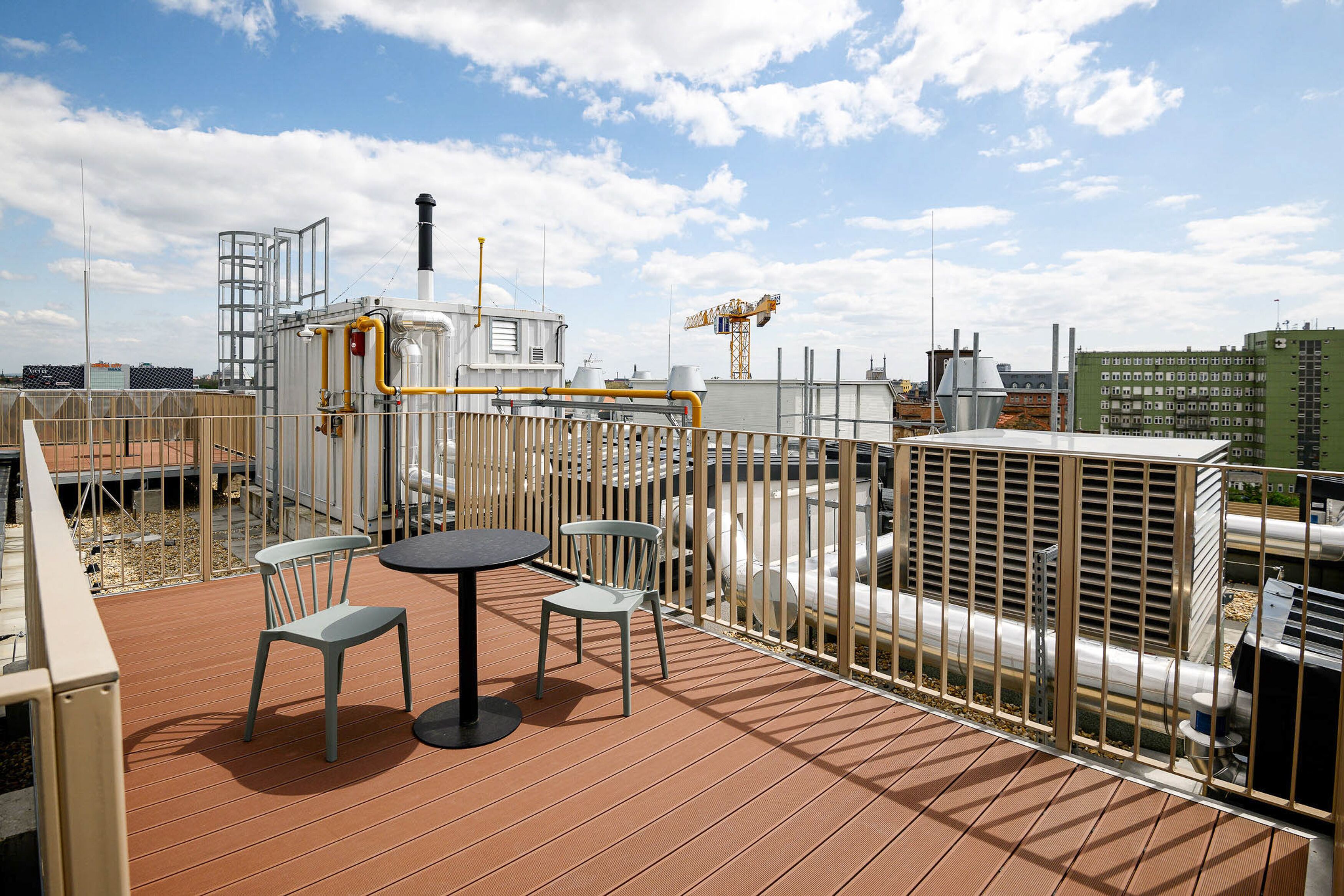 A rooftop terrace with a table and two chairs, surrounded by a metal fence.