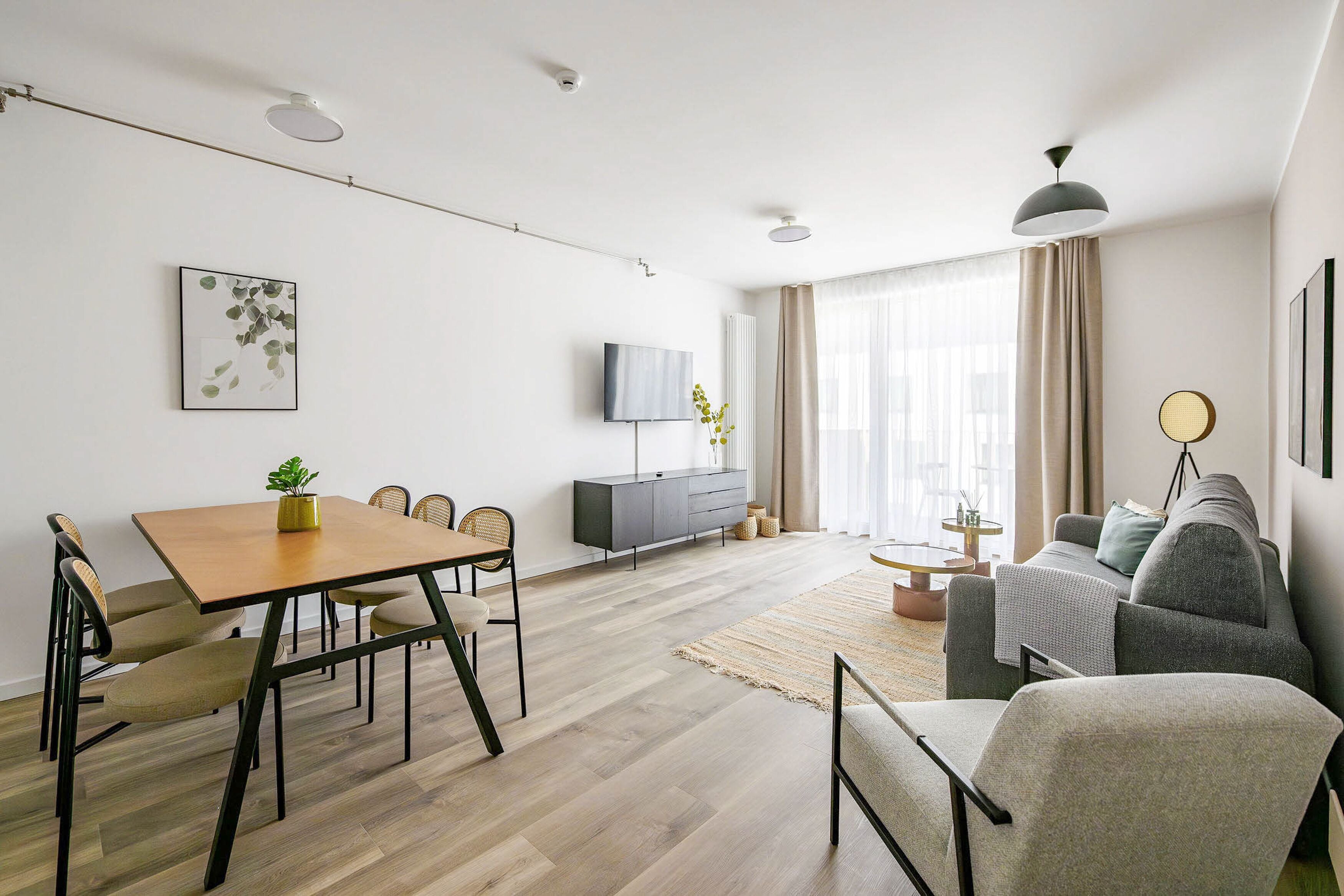 Ein modernes Wohnzimmer mit Essbereich, einem grauen Sofa, einem an der Wand montierten Fernseher und einem Holztisch mit Stühlen.