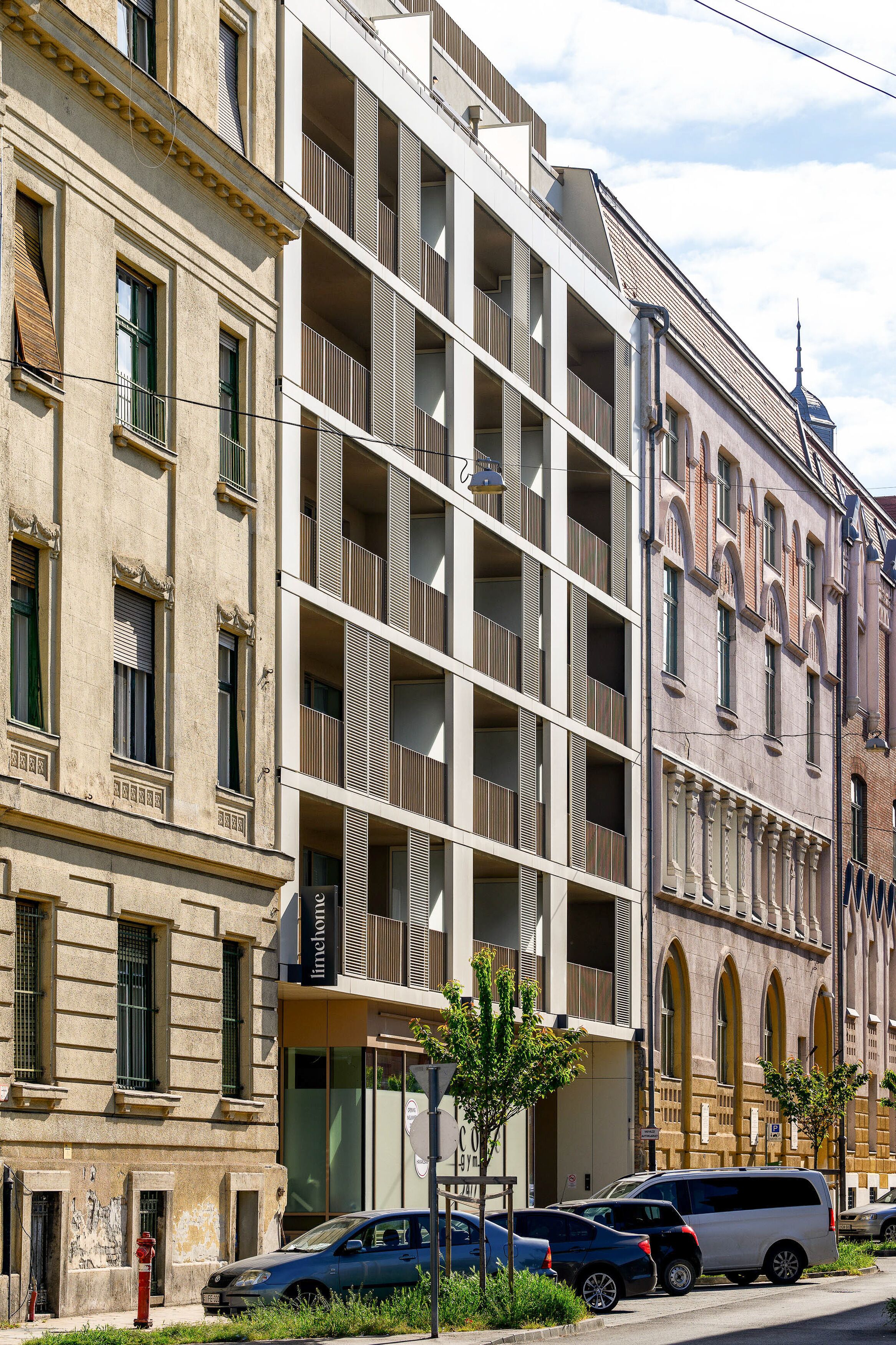 Un edificio de varios pisos con balcones, un hidrante y coches aparcados.