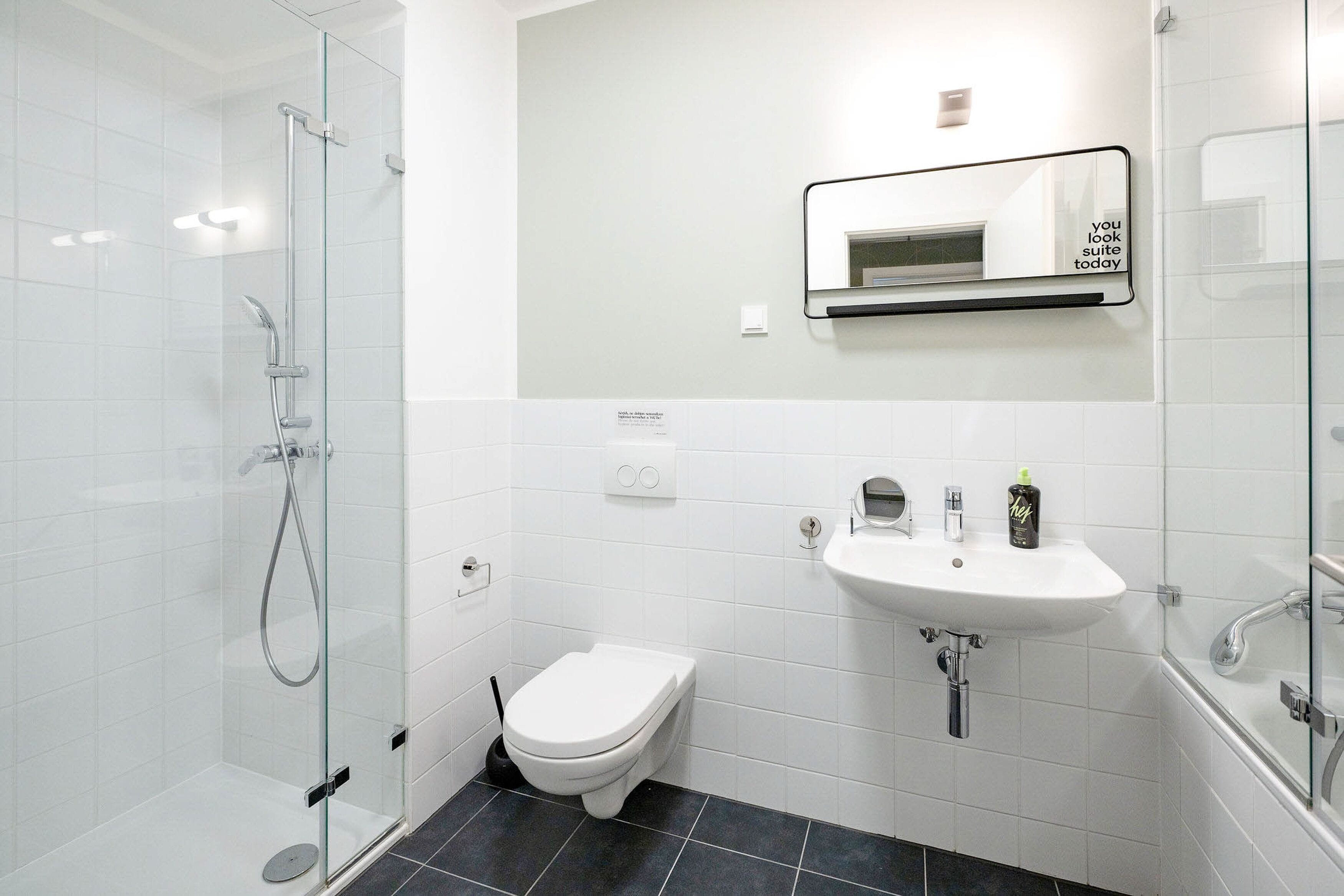 Un bany modern amb dutxa amb envàs de vidre, un vàter blanc, un lavabo i un mirall amb una frase motivacional.