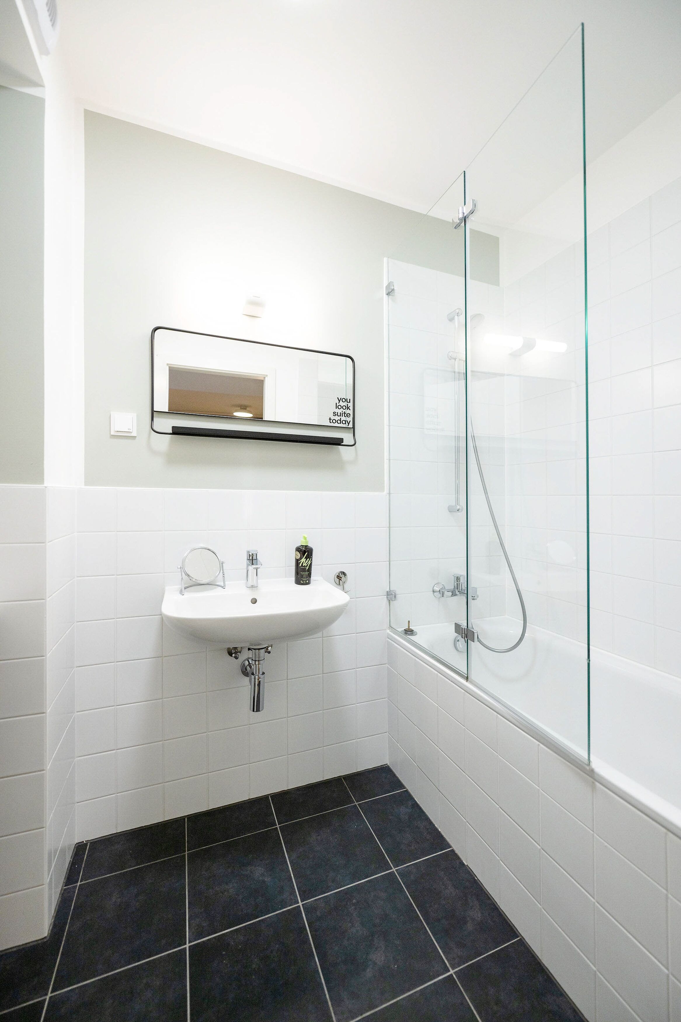 Un baño moderno con lavamanos blanco, espejo y cabina de ducha con mampara de vidrio.