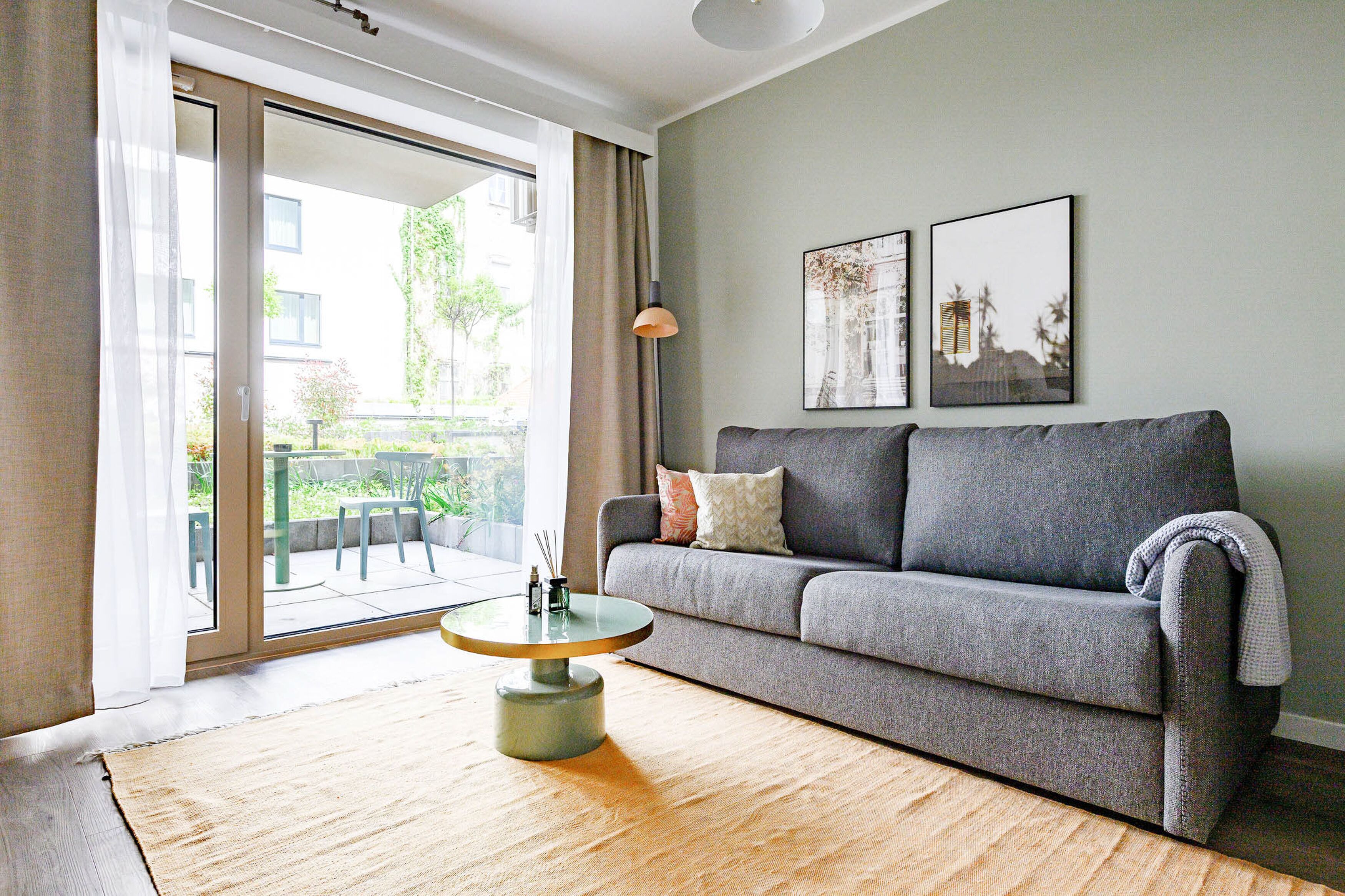Una sala de estar moderna con un sofá gris, una mesa de centro redonda y un amplio ventanal corredero que da a un espacio exterior.