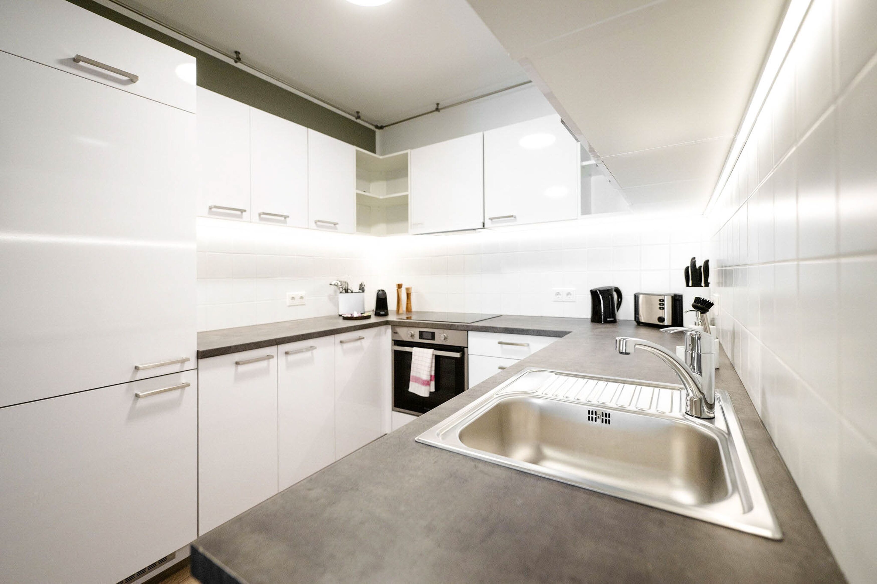 Una cocina moderna con armarios blancos, un lavamanos de acero inoxidable y un horno empotrado.