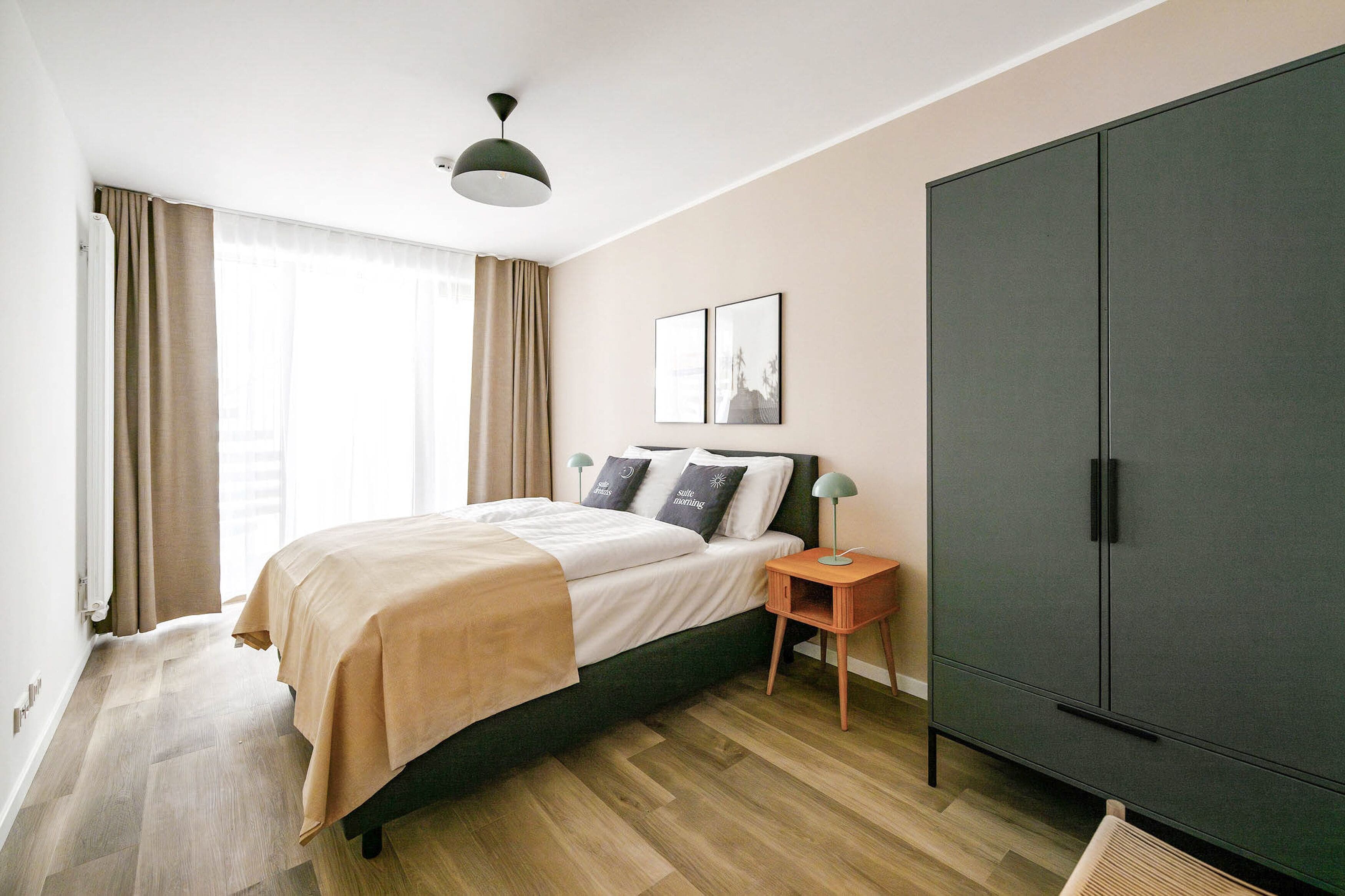 Un dormitorio con cama, armario, mesita de noche y una lámpara en el techo.