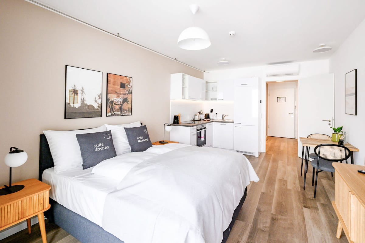 Quarto de hotel moderno com uma cama grande, uma escrivaninha e uma cozinha compacta.