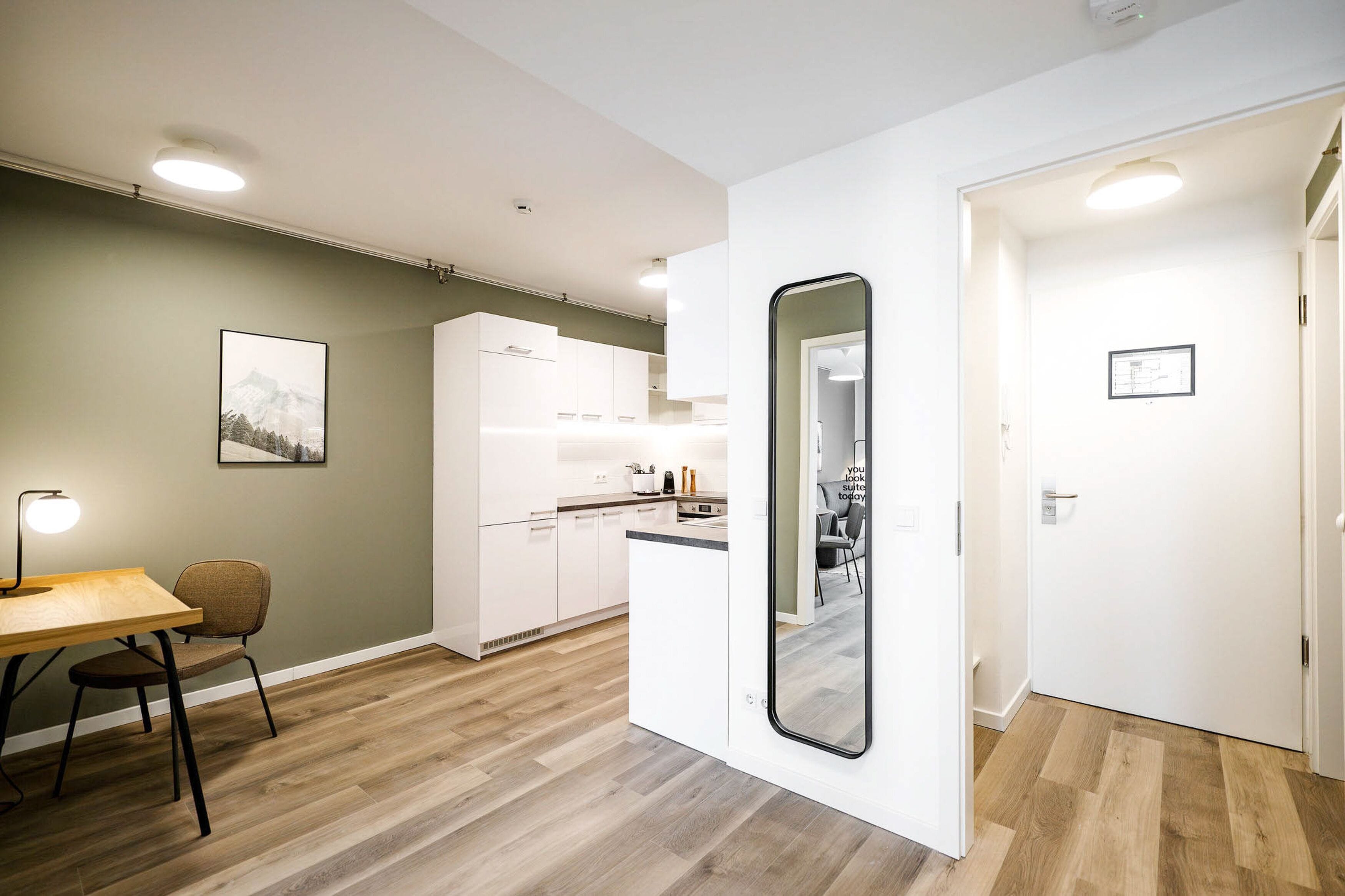 A modern kitchen with white cabinets, a dining area with a table and chairs, and a large mirror.