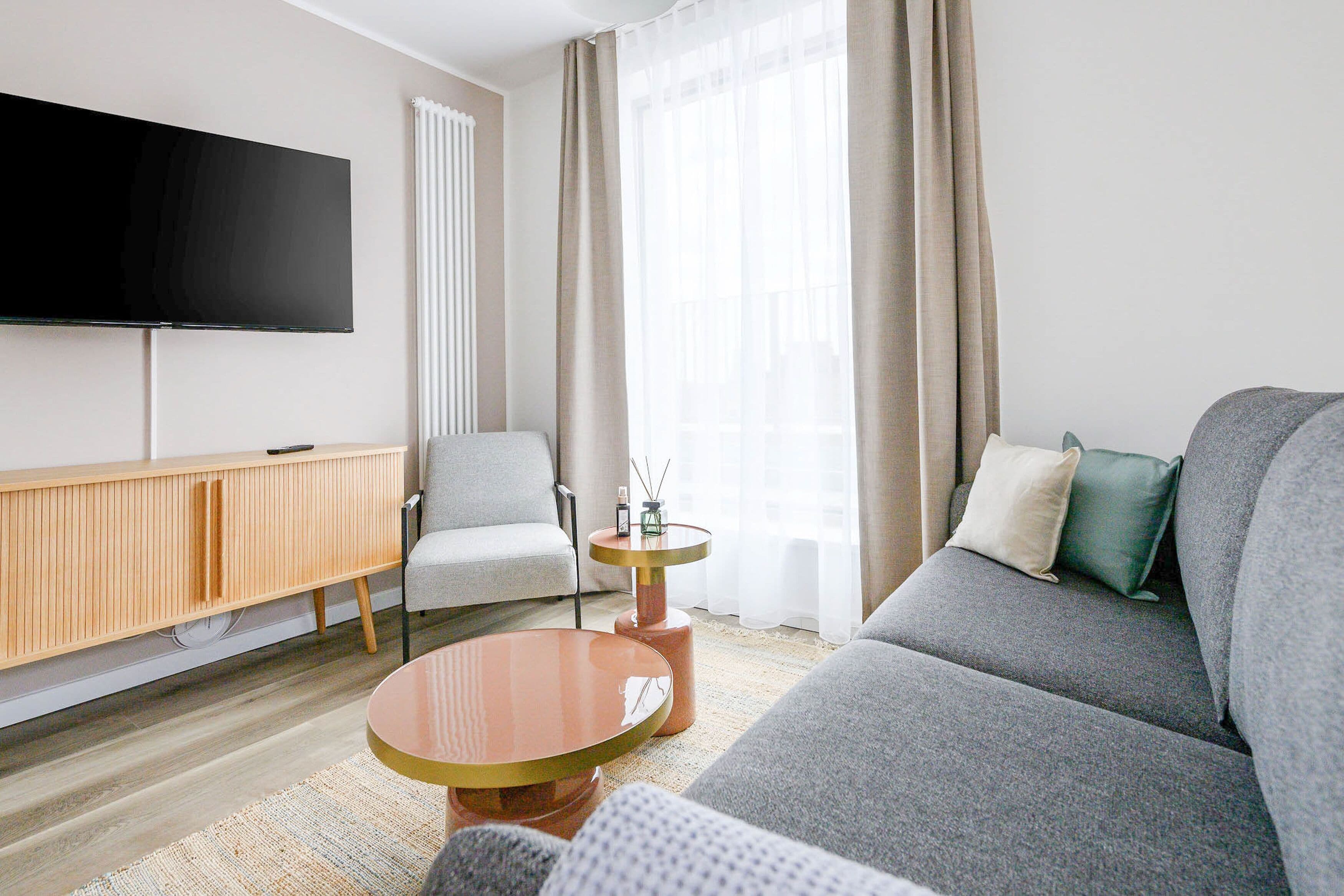 A modern living room with a flat-screen TV, a sofa, a chair, a small round table, and a wooden cabinet.