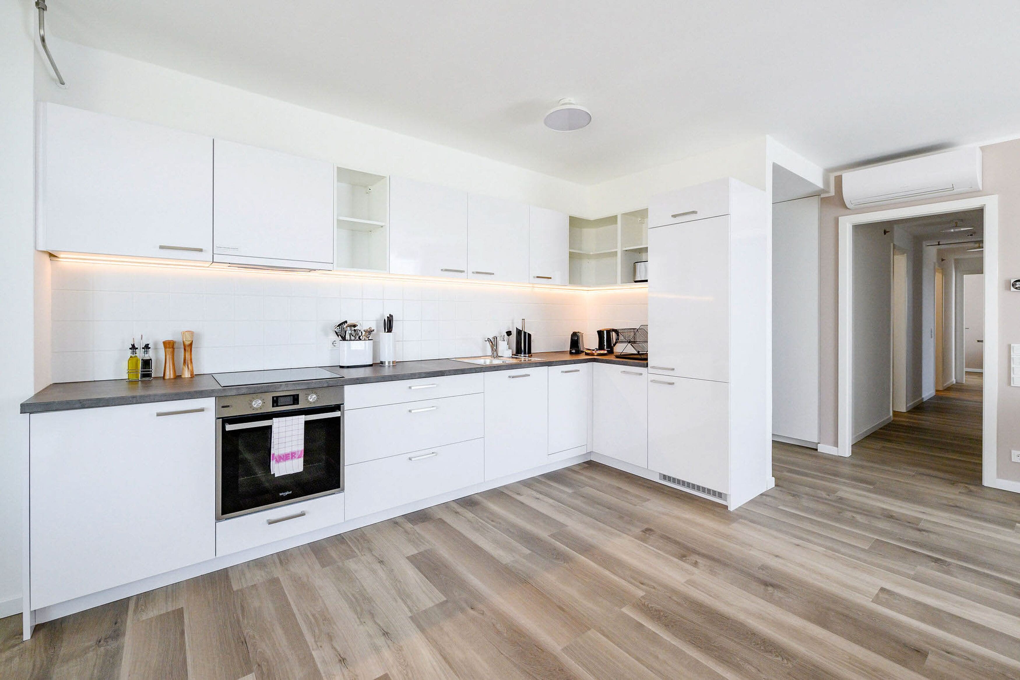 A modern kitchen with white cabinetry, a built-in oven, and a wooden floor.