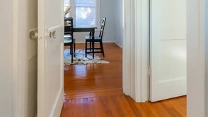 Un couloir avec un plancher en bois, un coin repas avec une table et des chaises, et une fenêtre avec des stores.