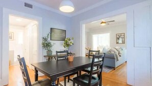 Un coin repas avec une table en bois foncé, quatre chaises, une plante en pot et un luminaire suspendu au plafond.
