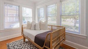 Une chambre à coucher avec un lit en bois, des murs blancs et de grandes fenêtres équipées de stores.