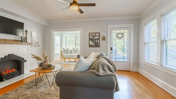 Un salon avec une cheminée, un canapé, un ventilateur de plafond et de grandes fenêtres.