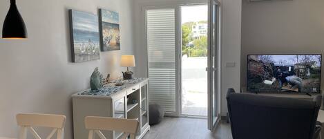A modern living room with a dining area, a TV, and a sliding glass door leading to an outdoor area.