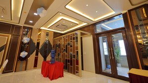 A modern hotel lobby with a red table, decorative lighting, and a view through a glass door. - Hotel Taj Crown Plaza (Agra)
