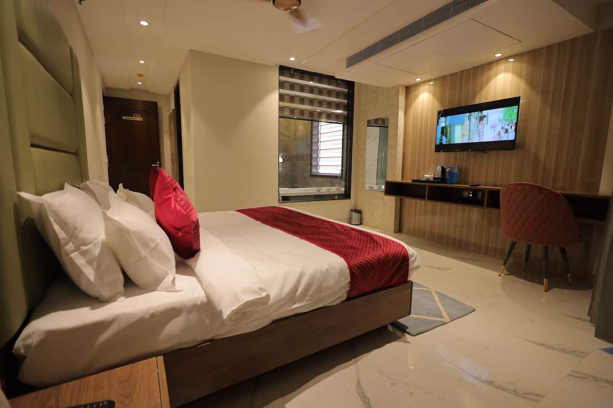 Una habitación de hotel moderna con una cama grande, un televisor montado en la pared, un escritorio con una silla y una ventana con persianas.