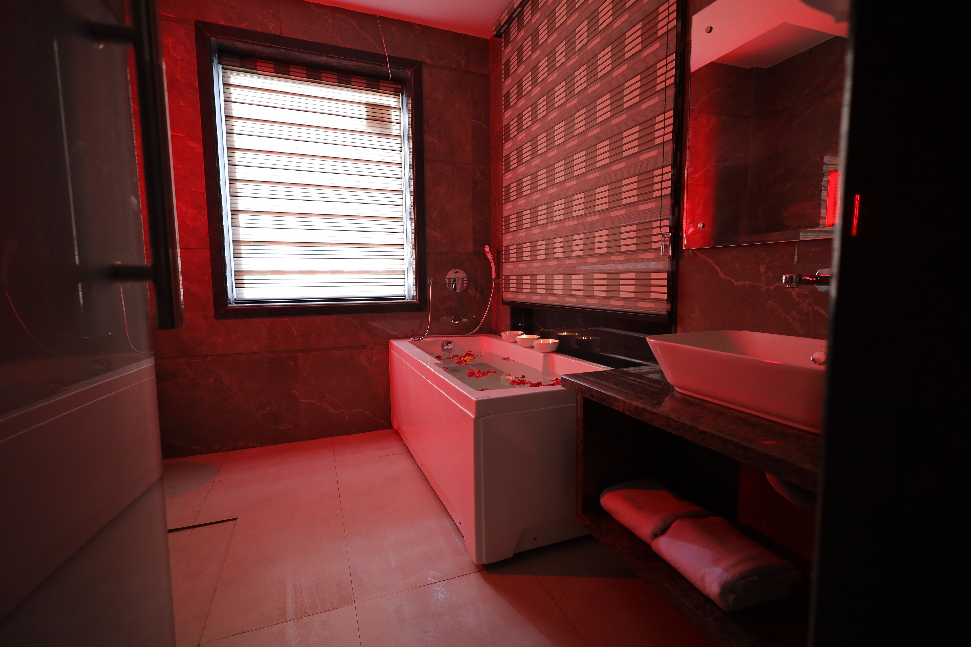 A modern bathroom with a white bathtub, a large mirror, and a red-toned wall.