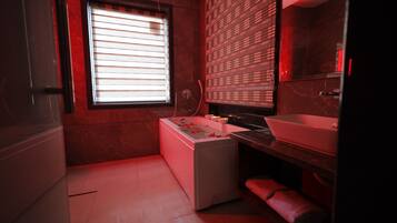 A modern bathroom with a white bathtub, a large mirror, and a red-toned wall.