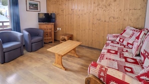 A living room with a wooden wall, a television, a sofa, two armchairs, and a coffee table.