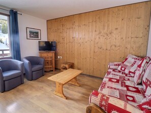 A living room with a wooden wall, a television, a sofa, two armchairs, and a coffee table.