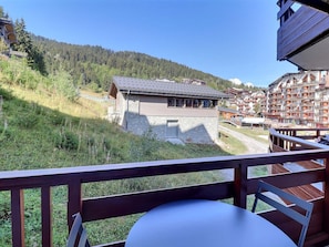 A mountain lodge with a stone facade, wooden deck, and a view of a forested hillside.