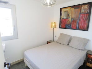 A bedroom with a bed, a nightstand, a lamp, and a painting on the wall.