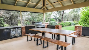 An outdoor patio with a grill, a table with benches, and a brick fireplace.