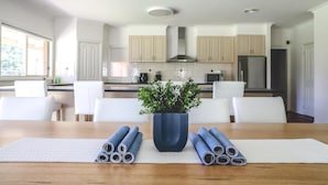 A modern kitchen with white cabinets, a central island with a potted plant, and rolled-up mats on the table.