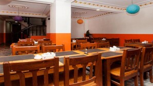 Un restaurante con mesas y sillas de madera, una escalera al fondo y detalles decorativos en el techo.