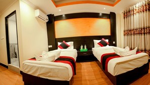 Habitación de hotel con dos camas, un televisor grande de montaje en pared y una cortina estampada con motivos florales.