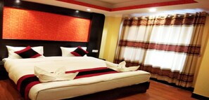 A hotel room with a large bed, a headboard with a red accent, and a window with patterned curtains. - MeroStay 229 Regency (Kathmandu)