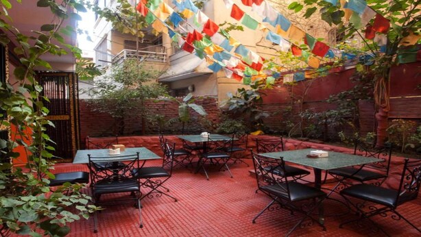 Un patio al aire libre con mesas y sillas, rodeado de muros de ladrillo y vegetación.