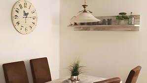 Ein Essbereich mit einem Marmortisch, braunen Stühlen, einer Uhr, einer Hängeleuchte und einem Regal mit Dekoration.