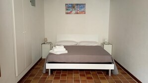 Ein Schlafzimmer mit einem Bett, weißen Nachttischen, einem Wandbild und einem Fliesenboden.