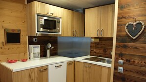 Cozinha compacta com armários de madeira, micro-ondas, cafeteira e uma decoração em formato de coração na parede.
