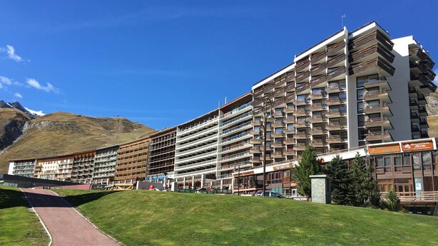 Um hotel de vários andares com varandas, uma placa de estação de esqui e montanhas ao fundo.