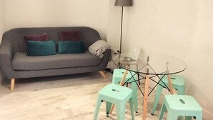Een woonkamer met een grijze bank, teal kussens, een klein glazen tafeltje met krukken en een vloerlamp.