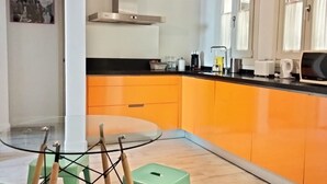 Een moderne keuken met oranje kastjes, een glazen tafel en een groene stoel.