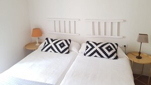 Een tweepersoonsbed met witte beddengoed en kussens met een zwart-wit patroon, een wit hoofdbord en twee nachtkastjes met lampen.