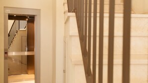 Une vue intérieure d’un couloir d’h ôtel, avec un ascenseur et un escalier visibles.