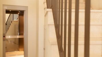 Ein Innenbereich zeigt einen Hotelkorridor mit einem sichtbaren Aufzug und einer Treppe.