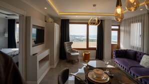 Een moderne hotelkamer met een groot raam, een flatscreen televisie, een bank, een eettafel met een vaas en een stoel.