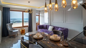 Een moderne woonkamer met een paarse bank, een eettafel voor vier personen en uitzicht op zee door grote ramen.