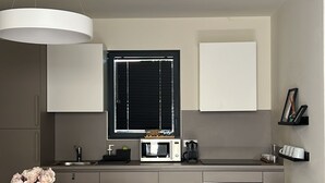 Una cocina moderna con una mesa redonda para comer, sillas blancas, horno empotrado, microondas y una ventana con persianas.