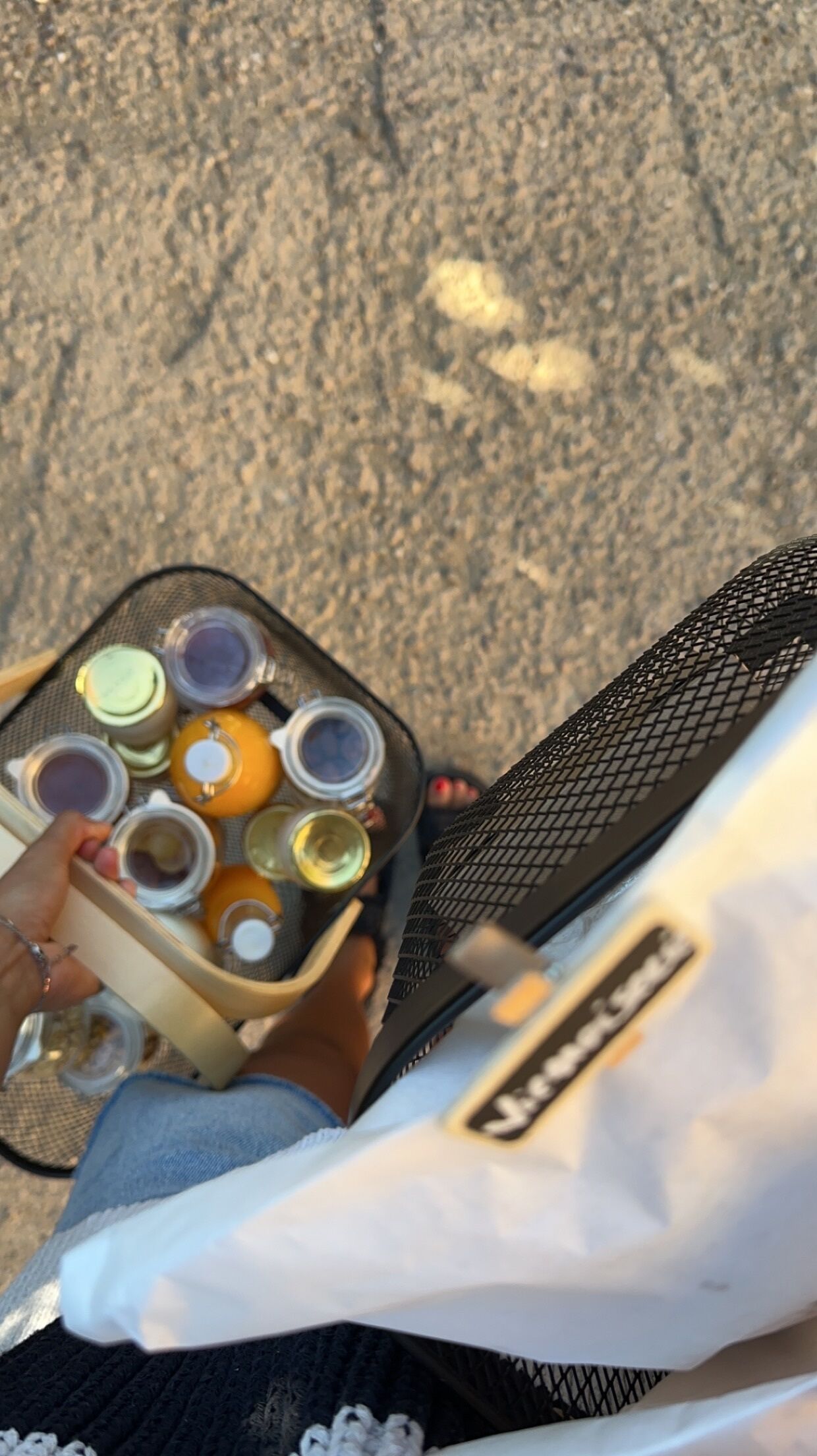 A person holding a tray with various containers, possibly food or drinks, on a textured surface.