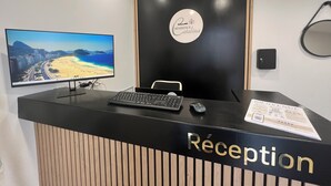Un mostrador de recepción con un monitor que muestra una escena de playa, un cartel que dice "Résidence Catalina" y un letrero de "Recepción" sobre el mostrador.