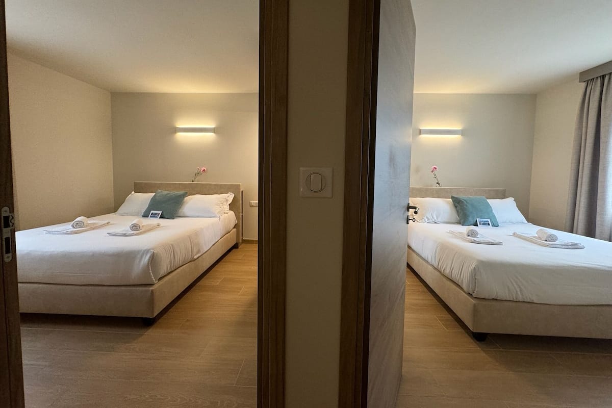 A hotel room with two beds, each with a pillow, a bedside table, and a wall-mounted light.