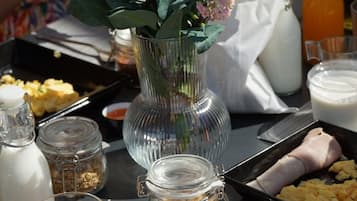 A breakfast table with a bowl of cereal, a glass of orange juice, a vase with flowers, and various food items.
