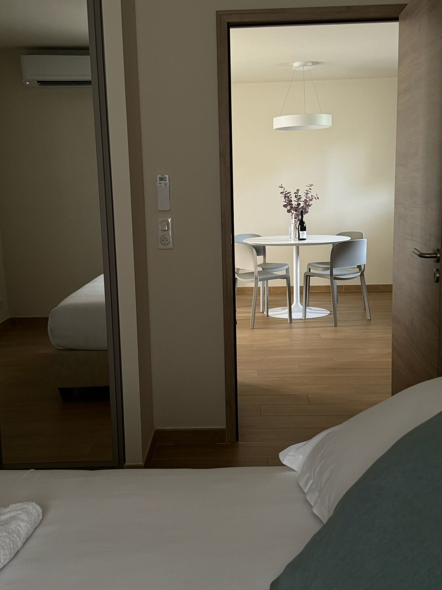 Una habitación de hotel con una cama, una pequeña mesa con sillas y un área de comedor visible a través de una puerta abierta.