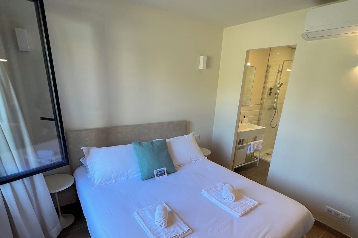 A hotel room with a bed, a bedside table, a mirror, and a bathroom visible through an open door.