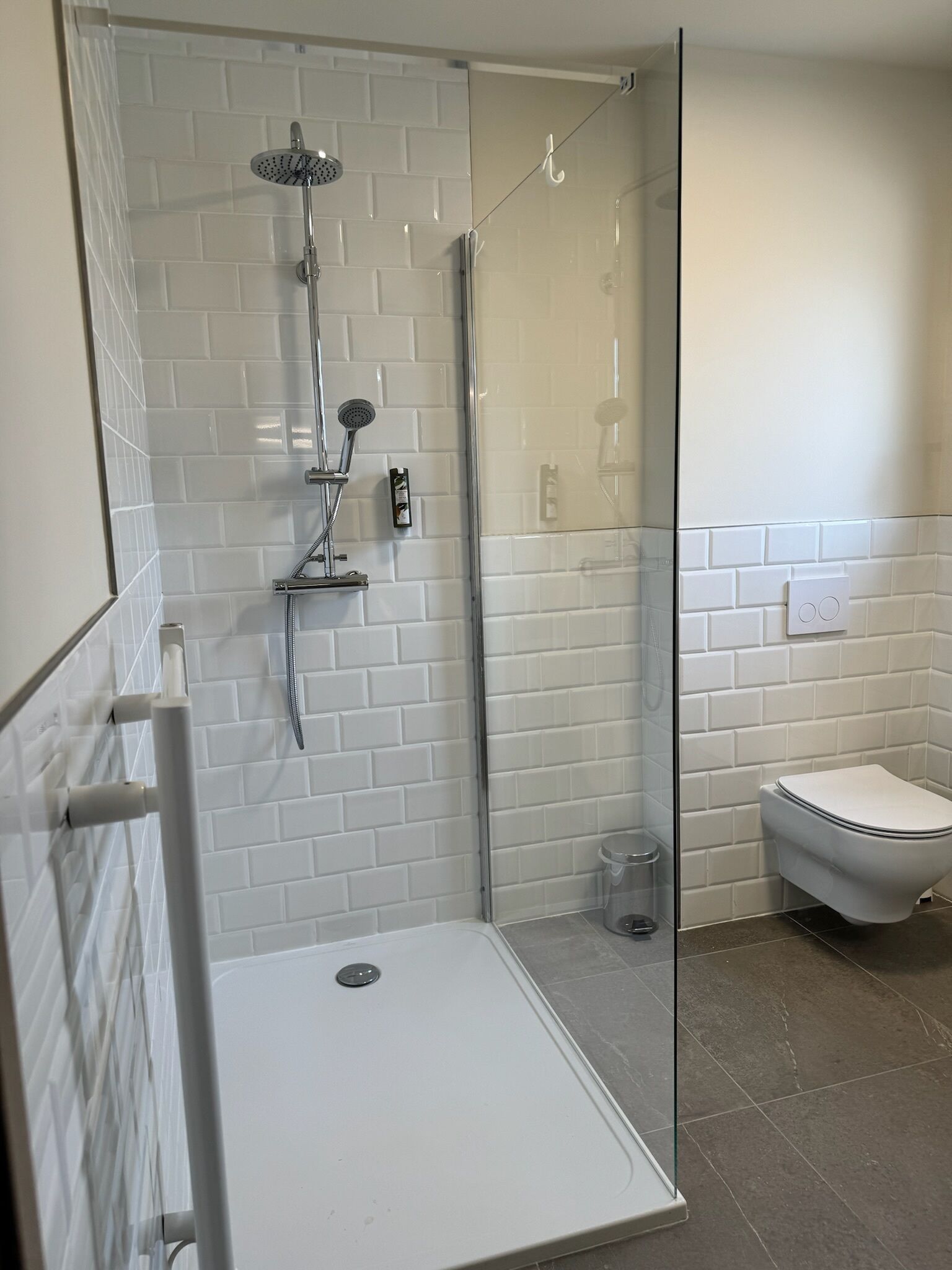 A modern bathroom with a glass-enclosed shower, white tiled walls, a white toilet, and a glass shower door.
